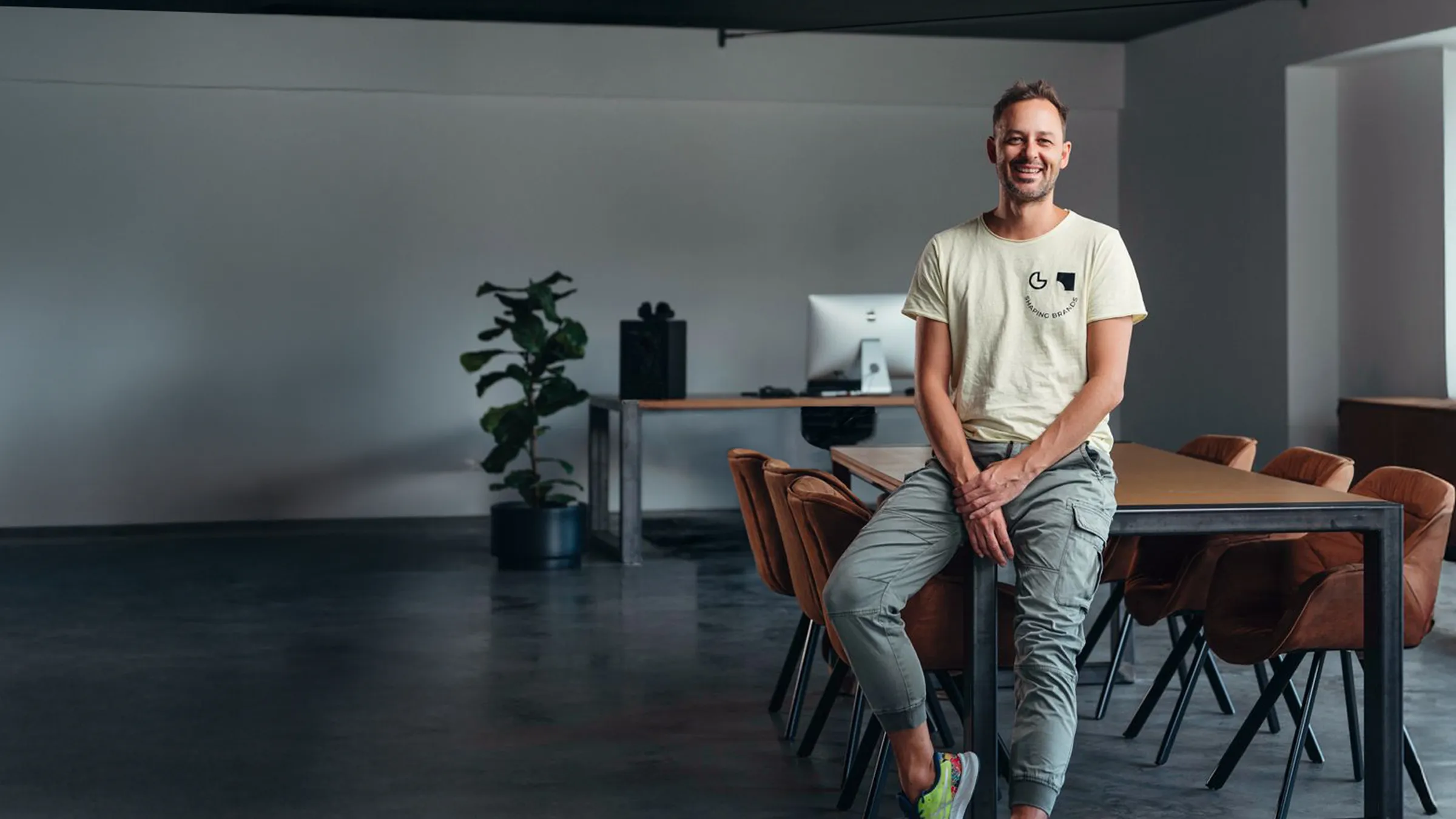 Dietmar Straubinger, Gründer von Lab7, sitzt lachend auf dem Besprechungstisch im Agenturbüro - Lead-Generierung und Ads von Lab7